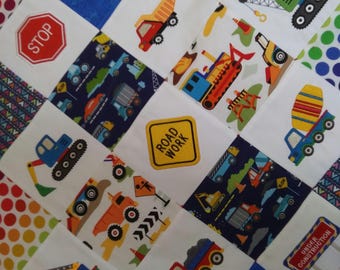 Puede incluir: Una colcha de retazos colorida con una variedad de diseños de vehículos de construcción. La colcha presenta una señal de stop, una señal de obras en la carretera y una señal de obras en curso. La colcha está hecha de diferentes telas, incluyendo azul, rojo, blanco y amarillo.
