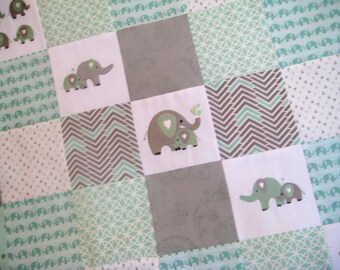 Puede incluir: Una colcha para bebé con un diseño de patchwork en varios tonos de verde y gris. La colcha está hecha de diferentes telas con varios patrones, incluyendo un patrón de chevron, un patrón geométrico y un patrón de elefantes pequeños. La colcha presenta elefantes bordados de varios tamaños.
