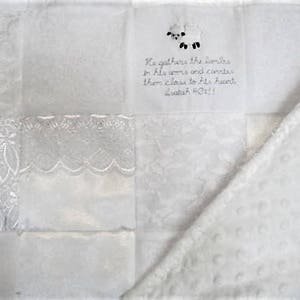 K&ouml;nnte beinhalten: Wei&szlig;e Babydecke mit Patchwork-Muster. Die Decke zeigt eine wei&szlig;e Lamm-Applikation und ein Zitat aus der Bibel: "Er sammelt die L&auml;mmer in seine Arme und tr&auml;gt sie nahe an sein Herz. Jesaja 40:11"