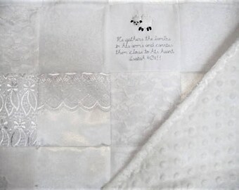 Puede incluir: Manta de bebé blanca con un diseño de patchwork. La manta presenta una aplicación de cordero blanco y una cita de la Biblia: "Reúne los corderos en sus brazos y los lleva cerca de su corazón. Isaías 40:11"