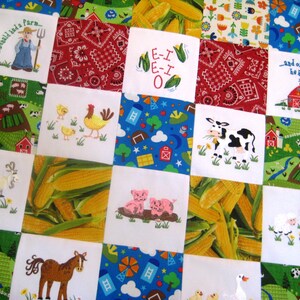 May include: A colorful quilt with a farm theme. The quilt is made up of squares with different images, including a red barn, a cow, corn, a rooster, and a pig. The quilt is perfect for a child's room or nursery.