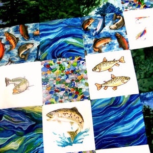 May include: A quilt with a patchwork design featuring various images of fish, including trout, bass, and catfish. The quilt is made of different fabrics with a blue and green color scheme.