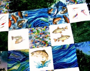 Puede incluir: Una colcha con un diseño de patchwork que presenta varias imágenes de peces, incluyendo truchas, lubinas y bagres. La colcha está hecha de diferentes telas con una combinación de colores azul y verde.