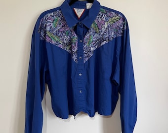 May include: A blue long-sleeved button-down shirt with a floral print on the yoke and cuffs. The shirt has a pointed collar and a single button closure at the neck. The brand label reads "Cowgirls Rodeo".