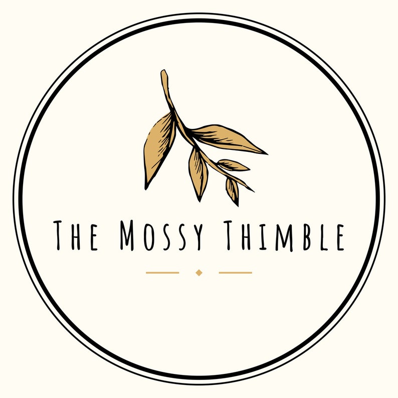 May include: A white circle with a black outline and a gold branch with leaves in the center. The text "THE MOSSY THIMBLE" is written below the branch.