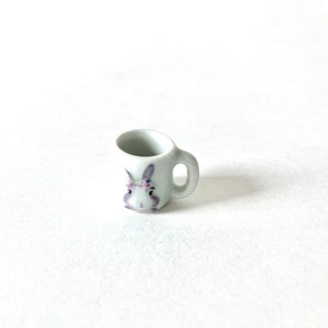 May include: A white ceramic mug with a purple bunny face design. The bunny has a flower crown on its head.