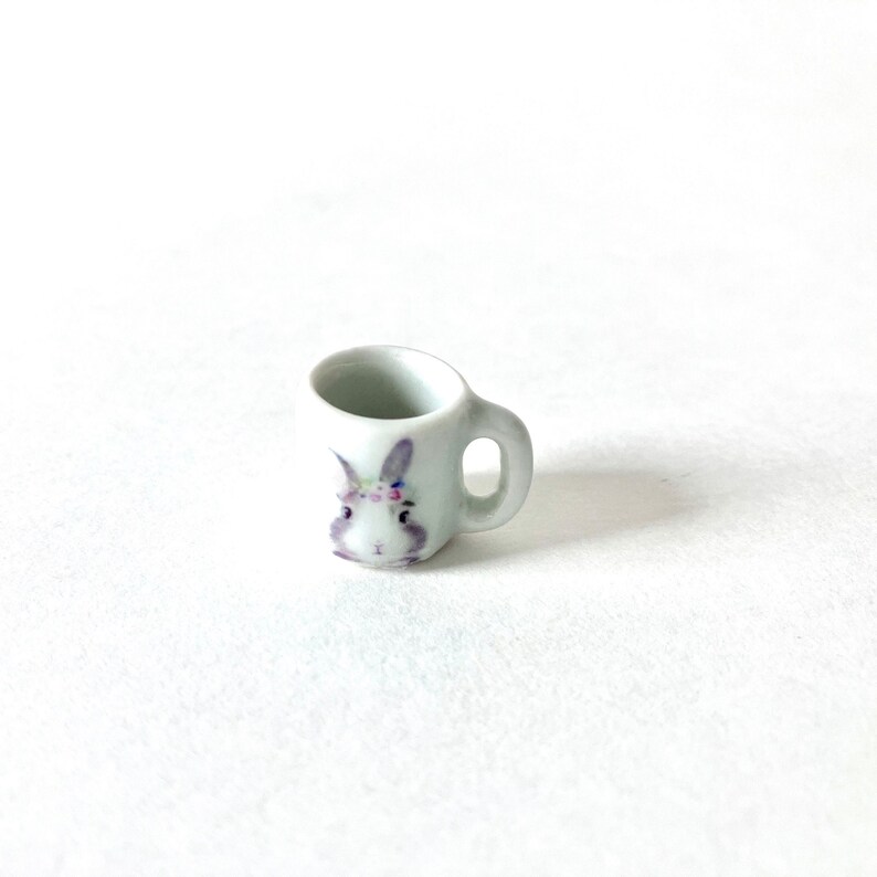 May include: A white ceramic mug with a purple bunny face design. The bunny has a flower crown on its head.