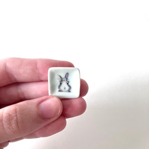 May include: A small white square ceramic dish with a floral crown bunny illustration.