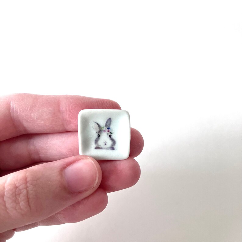 May include: A small white square ceramic dish with a floral crown bunny illustration.