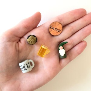 May include: A collection of five miniature items: a green gnome, a white mug with the word "LUCKY" on it, a yellow beer mug, a small pile of gold coins, and a copper penny with the word "Lucky" engraved on it.