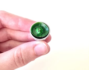 May include: A green thimble with a ladybug design. The ladybug is black with white spots and is centered on the top of the thimble.
