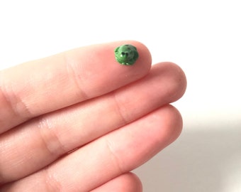 May include: A small green frog figurine, about the size of a fingernail, is held in a person's hand.