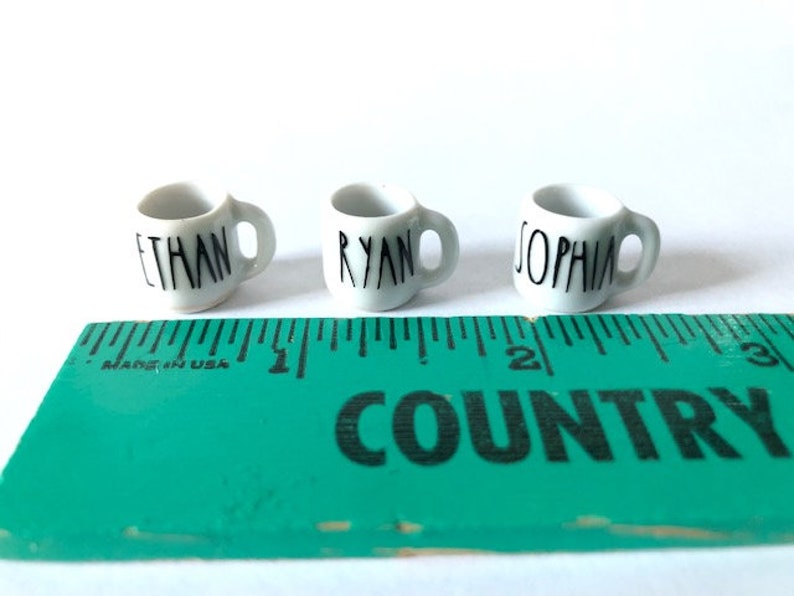 May include: Three white ceramic mugs with black lettering. The mugs are labeled "Ethan", "Ryan", and "Sophia".