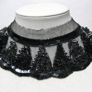 May include: Black beaded collar necklace with a scalloped edge. The collar features a sheer black mesh base, embellished with sequins and beads. The design includes a band of black sequins and a decorative fringe.