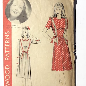 Peut inclure: Enveloppe vintage Wood Patterns avec des illustrations de robes. Une robe est rouge à pois blancs, l'autre est à carreaux gris avec des accents rouges. Comprend un portrait d'Adele Mara.