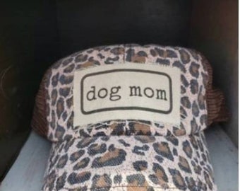 May include: A brown and white leopard print trucker hat with a white patch that says "dog mom" in black text.
