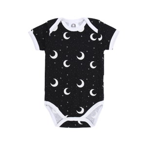 Könnte beinhalten: Schwarzer Baby-Body mit weißem Mond- und Sternenmuster. Der kurzärmelige Body hat weiße Einfassungen an Ausschnitt, Ärmeln und Beinen. Für Babys und Kleinkinder.