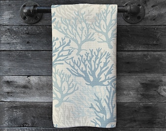 May include: A white kitchen towel with a blue coral reef pattern. The towel is hanging on a black metal towel rack.