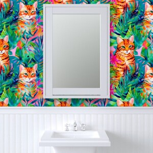 May include: A white bathroom vanity with a mirror above the sink. The walls are covered in a colorful wallpaper featuring orange cats and tropical leaves.