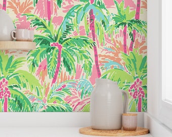 May include: A white kitchen with a wallpaper featuring a tropical palm tree pattern in shades of green, pink, and blue. A white pitcher and a small brown jar are on a wooden coaster on a white countertop.