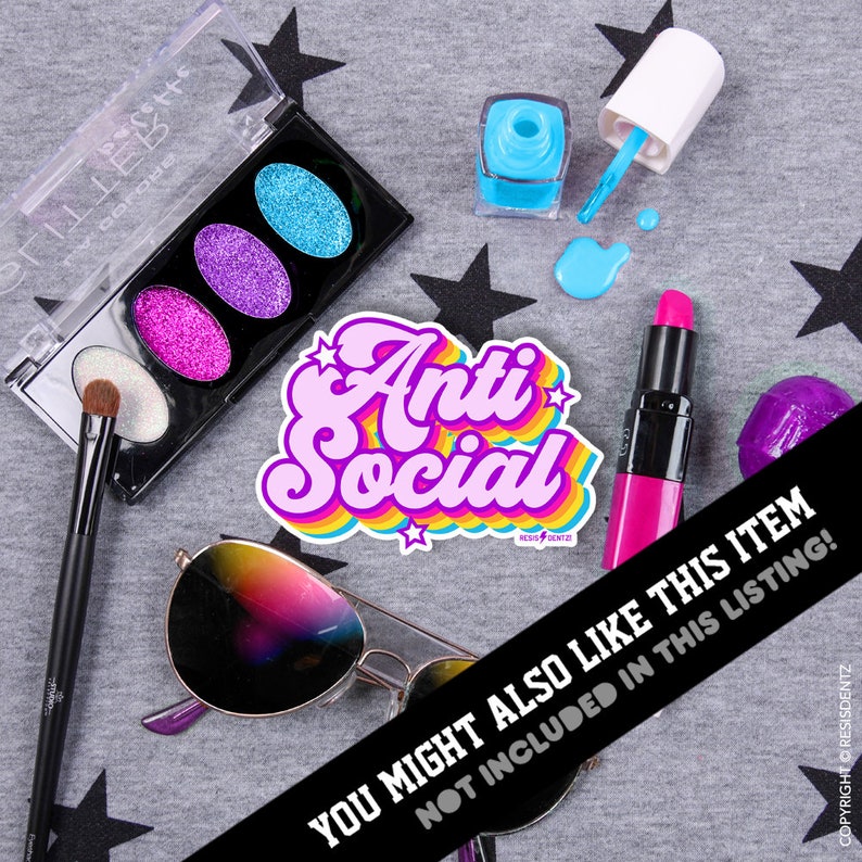 Op de afbeelding: Een roze en regenboogkleurige sticker met de tekst "Anti Social" in een retro-lettertype. De sticker is omringd door verschillende make-upartikelen, waaronder een palet met glitter-oogschaduw, een buisje lippenstift en een flesje nagellak.