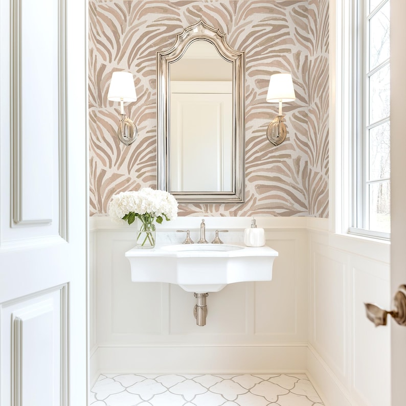May include: A white bathroom vanity with a white porcelain sink and chrome faucets. The vanity is in a small bathroom with white walls and a patterned wallpaper featuring a zebra print in shades of brown and beige. The bathroom also has a large mirror with a silver frame and a white tiled floor.
