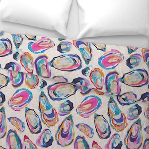 May include: A cream-colored bedspread with a repeating pattern of colorful oyster shell illustrations. The shells are painted with vibrant hues of pink, blue, orange, and purple, creating a lively and artistic design. The bedspread is paired with white pillows.