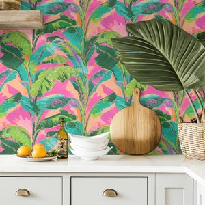 May include: A vibrant kitchen scene featuring a colorful tropical wallpaper with large banana leaves in shades of green, pink, and teal. A wooden cutting board, white bowls, and a bottle of wine are on the countertop. Oranges and a plant are also visible.