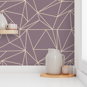 Puede incluir: Un papel tapiz geométrico morado con un patrón geométrico blanco. Una jarra blanca y un pequeño frasco blanco están sobre una posavasos de madera en una encimera blanca.