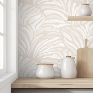 May include: A white ceramic kitchen countertop with a white and beige patterned wallpaper. There are three white ceramic containers on the counter, two with lids and one without. A wooden cutting board is leaning against the back wall.