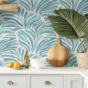 May include: A kitchen countertop with white cabinets and a blue and white zebra print wallpaper. There is a wooden cutting board, a glass bottle, a plate of lemons, and a stack of white bowls on the counter.