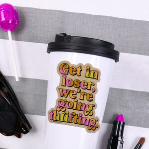 Op de afbeelding: Witte reistumbler met een bruine en roze sticker met de tekst "Get in loser, we're going thrifting."
