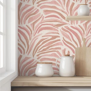 May include: A kitchen countertop with a pink and brown zebra print wallpaper. There are two white ceramic canisters and a white ceramic pitcher on the countertop.