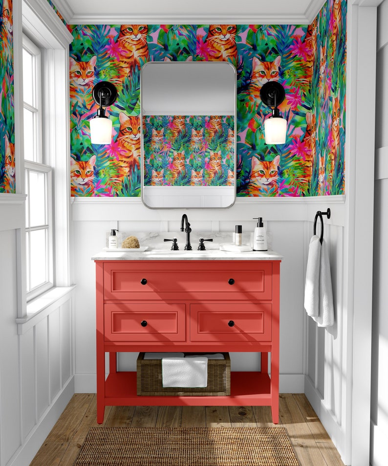 May include: A red bathroom vanity with three drawers and a bottom shelf. The vanity has a white countertop with a black faucet and a white ceramic sink. The wall behind the vanity is covered in wallpaper with a pattern of orange cats and tropical leaves.
