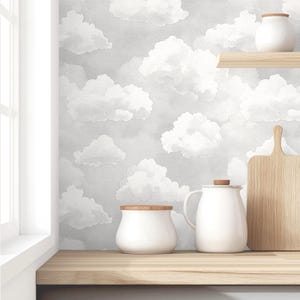 May include: A kitchen scene featuring a light wood countertop and a gray cloud-patterned wallpaper. White ceramic jars, a teapot, and a wooden cutting board are arranged on the counter. A window is visible on the left.