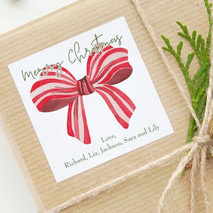 May include: A wrapped gift with a white label featuring a watercolor red and white striped bow and the words "Merry Christmas" in green script. The label also includes the names Richard, Liz, Jackson, Sara, and Lily. The gift is tied with twine.