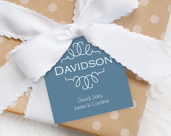 May include: A blue gift tag with white lettering that reads "DAVIDSON" with a decorative design above and below the name. The tag also includes the text "David Sara, James & Caroline". The tag is tied to a brown gift box with white polka dots and a white ribbon with scalloped edges.