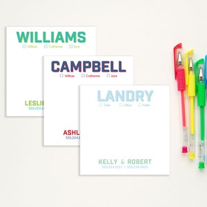 May include: Five white notepads with different names printed in colorful letters. The names are Williams, Campbell, Landry, Ashley, and Kelly & Robert. Each notepad has a phone number printed below the name. The notepads are arranged in a vertical stack on a white surface.