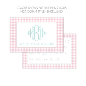 May include: A pink and white gingham card with a light blue monogram "MRA" and the text "MARY ANNE ROGERS". The card is for practicing writing the alphabet, with dotted lines for each letter.