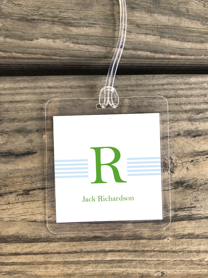 May include: A white luggage tag with a green letter "R" and three blue stripes. The text "Jack Richardson" is printed below the letter.