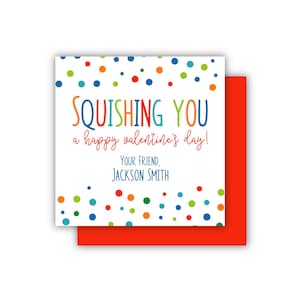 May include: A Valentine's Day card with the message "Squishing You a Happy Valentine's Day!" in colorful text. The card has a white background with scattered colorful polka dots and is layered over a red card.
