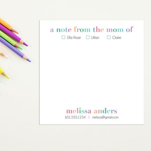 May include: A white note card with the text "a note from the mom of" in rainbow colors. There are three checkboxes below the text, labeled "Ella Rose", "Lillian", and "Claire". The bottom of the card has the text "melissa anders" in rainbow colors, followed by a phone number and email address.