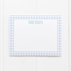 May include: A white card with a blue and white gingham border. The text "Teddy Roberts" is printed in green at the top of the card.