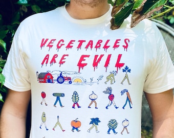 May include: White t-shirt with the text "VEGETABLES ARE EVIL" in red dripping letters. The shirt features a cartoon illustration of a farm scene with a red tractor, a barn, and a variety of vegetables walking with human legs.