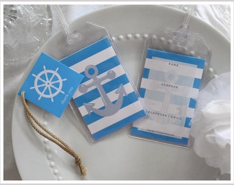May include: Clear plastic luggage tags with blue and white nautical designs. One tag features an anchor, another has a blue square tag with a ship's wheel and the words "thank you". The tags are on a white plate.