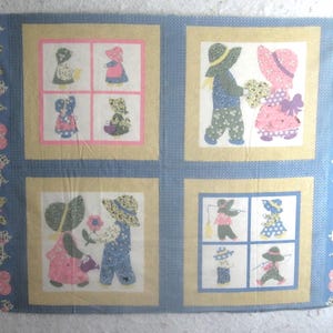 May include: A rectangular fabric panel featuring four distinct sections with illustrations of children in bonnets and hats. The border is blue with white butterfly and heart patterns. The central squares are framed in yellow and blue with floral motifs.