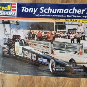May include: A Revell Monogram model kit box featuring Tony Schumacher's Top Fuel Dragster. The box art shows the dragster in action, with the text "Blues Are Back" and "Hollywood" visible. The kit is 1:25 scale and for ages 12 and up.