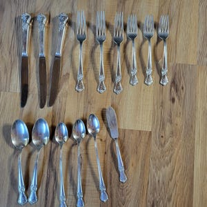 May include: A set of silverware, including forks, knives, and spoons, all made of silver. The silverware is arranged on a wooden surface.