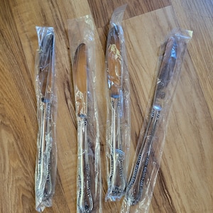 May include: Four silver butter knives with ornate handles are individually packaged in clear plastic.
