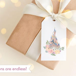 May include: A white gift tag with a watercolor illustration of a pink and blue castle with a floral wreath around the base. The tag is tied to a brown gift box with a white ribbon.